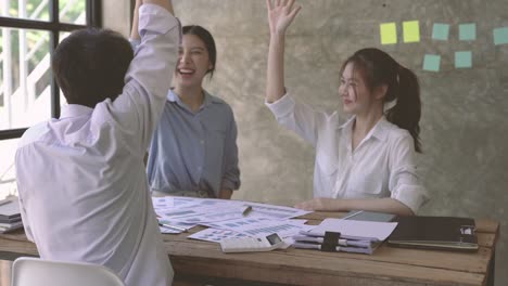 group of young adult asian business people join hands stacking and clap together in team meeting.