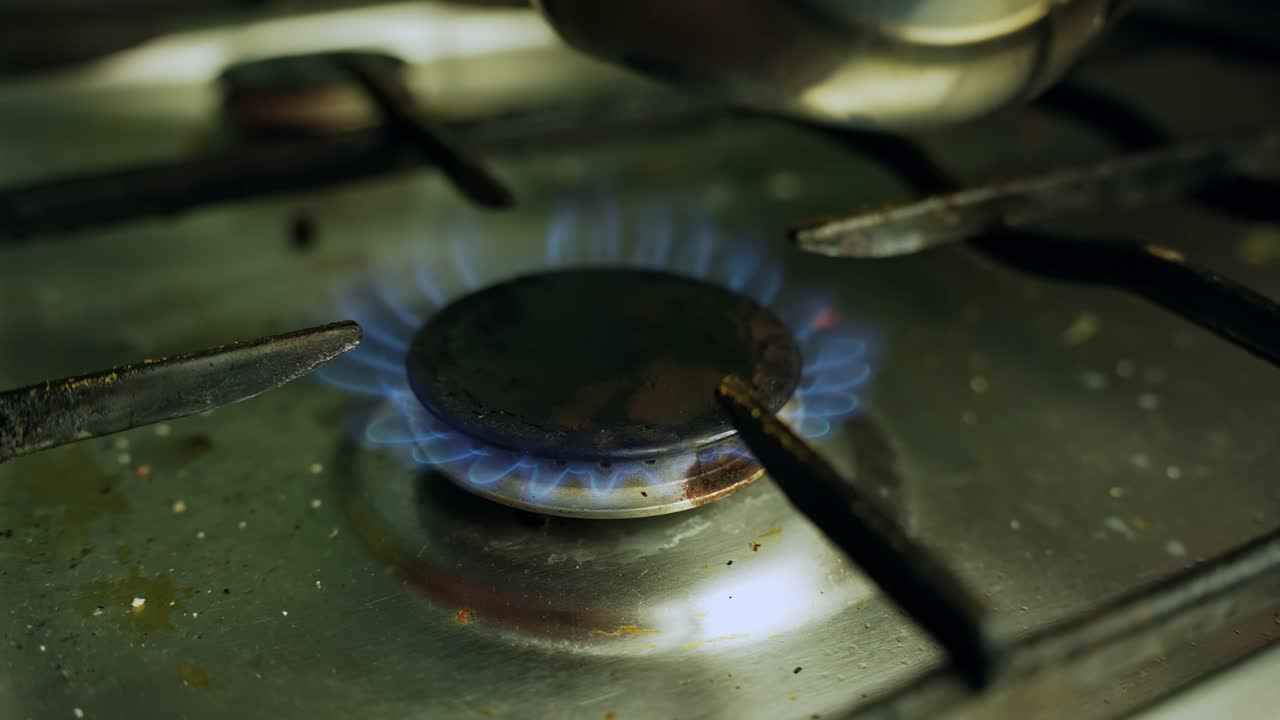 Primo piano di una fiamma di gas blu che si accende su un piano cottura sporco, bruciatore che si illumina su una cucina casalinga per il concetto di calore ed energia per cucinare