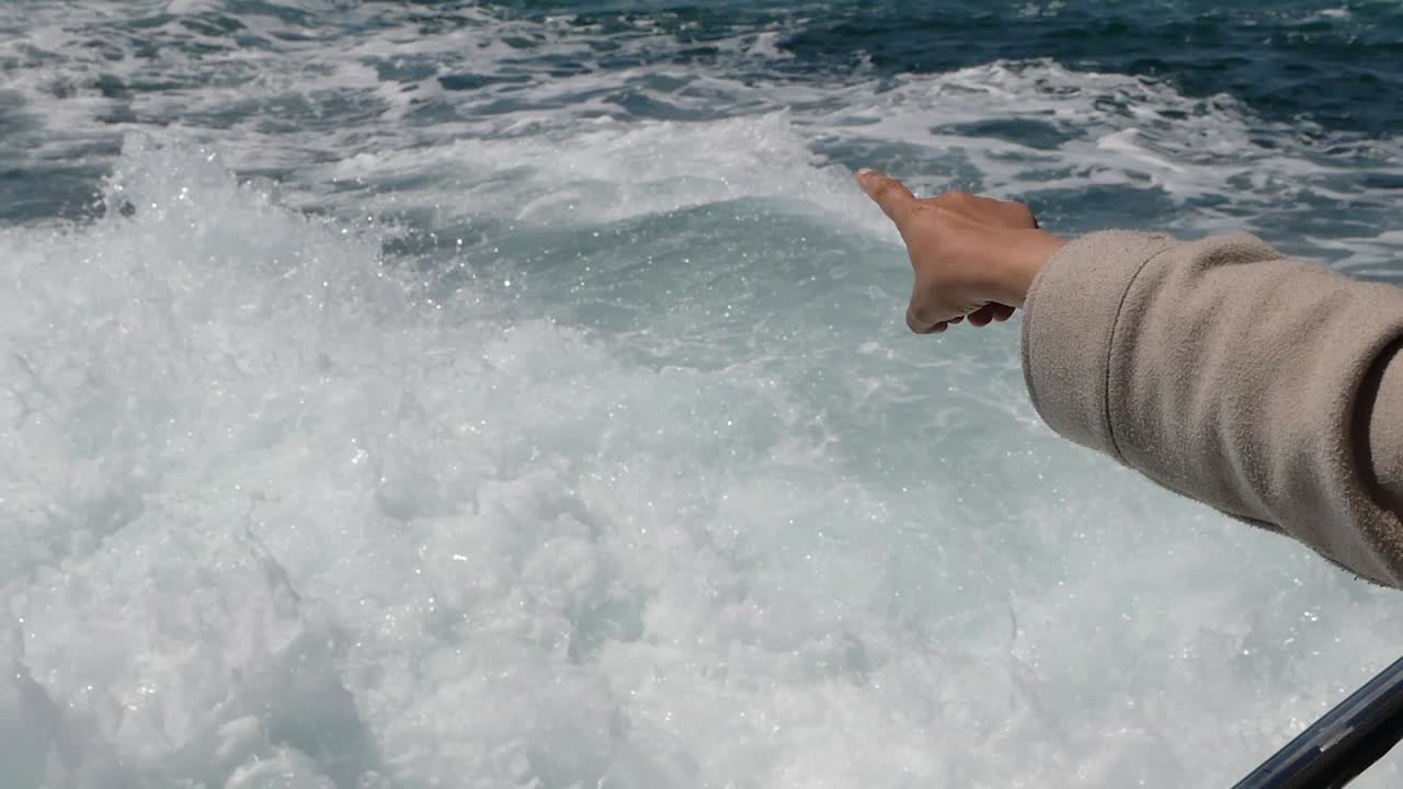 Hand pointing at the boat wake on the ocean