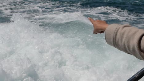 hand pointing at the boat wake on the ocean