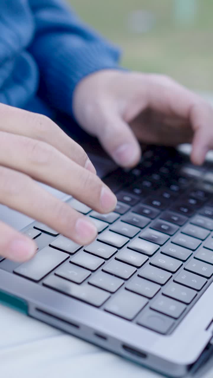 Programmer writing code on laptop keyboard outdoors. Vertical