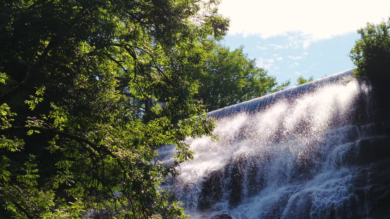 Sunlit waterfall in Italian Alps with lush green trees, calming nature