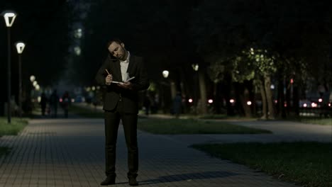 businessman using smart phone make a call while standing at park in a city square, and make notes