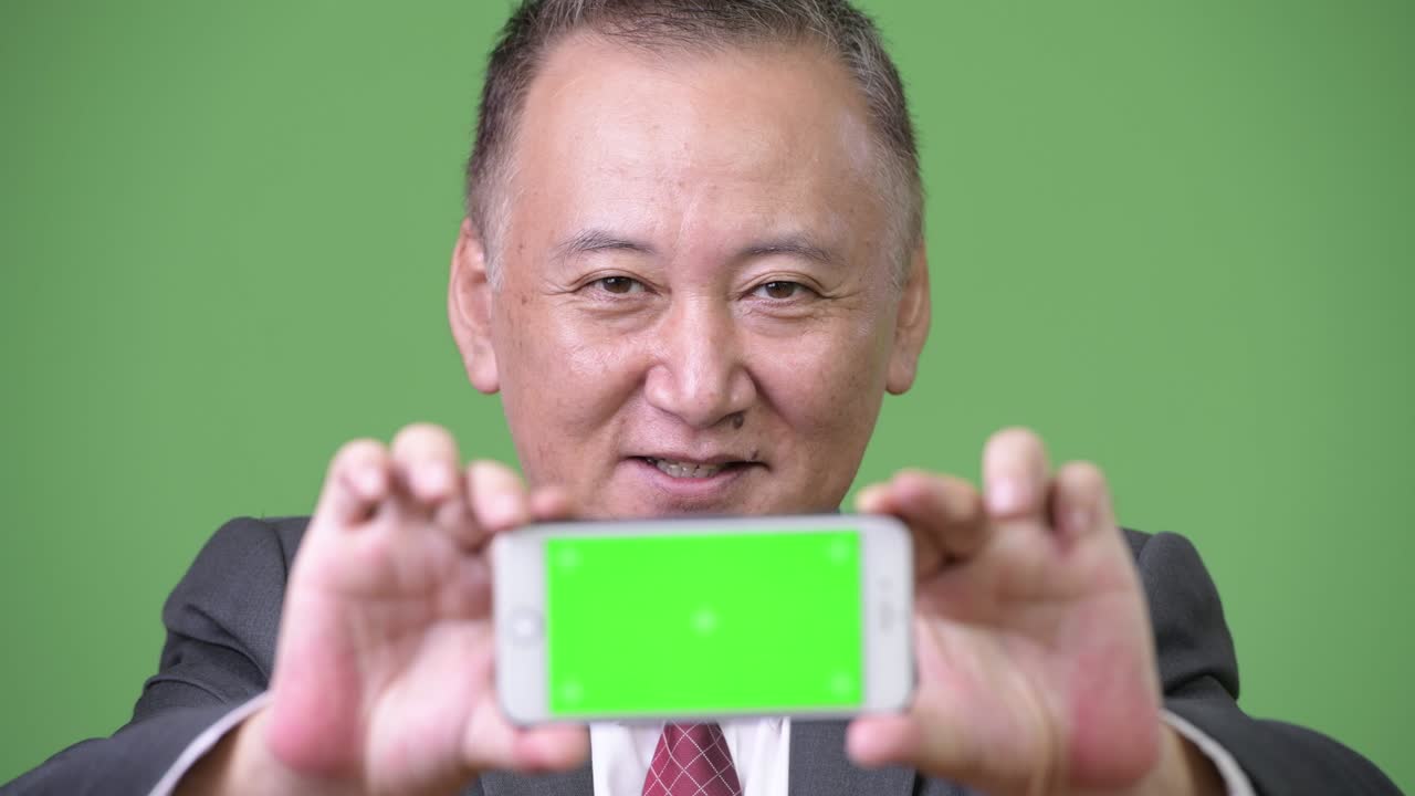 성숙 한 일본인 사업가 가 카메라 에 전화 를 보여주고 있다