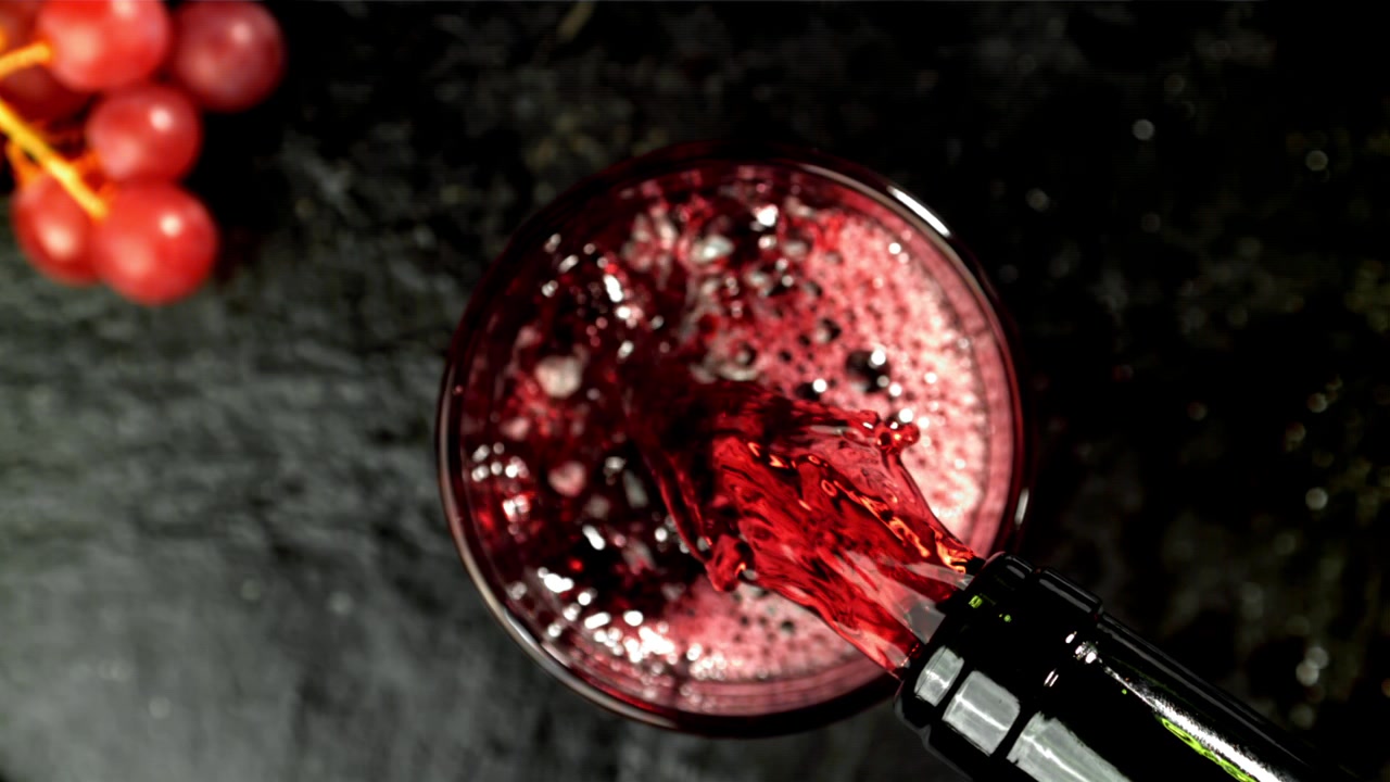 Vino rosso che si versa in un bicchiere al rallentatore, vista dall'alto.