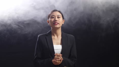 asian speaker woman in business suit showing index fingers up while speaking in the black screen studio