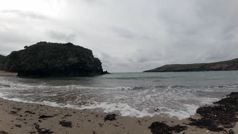 Slow-motion-tide-crashing-on-sandy-UK-beach-with-island-mountains-across-horizon