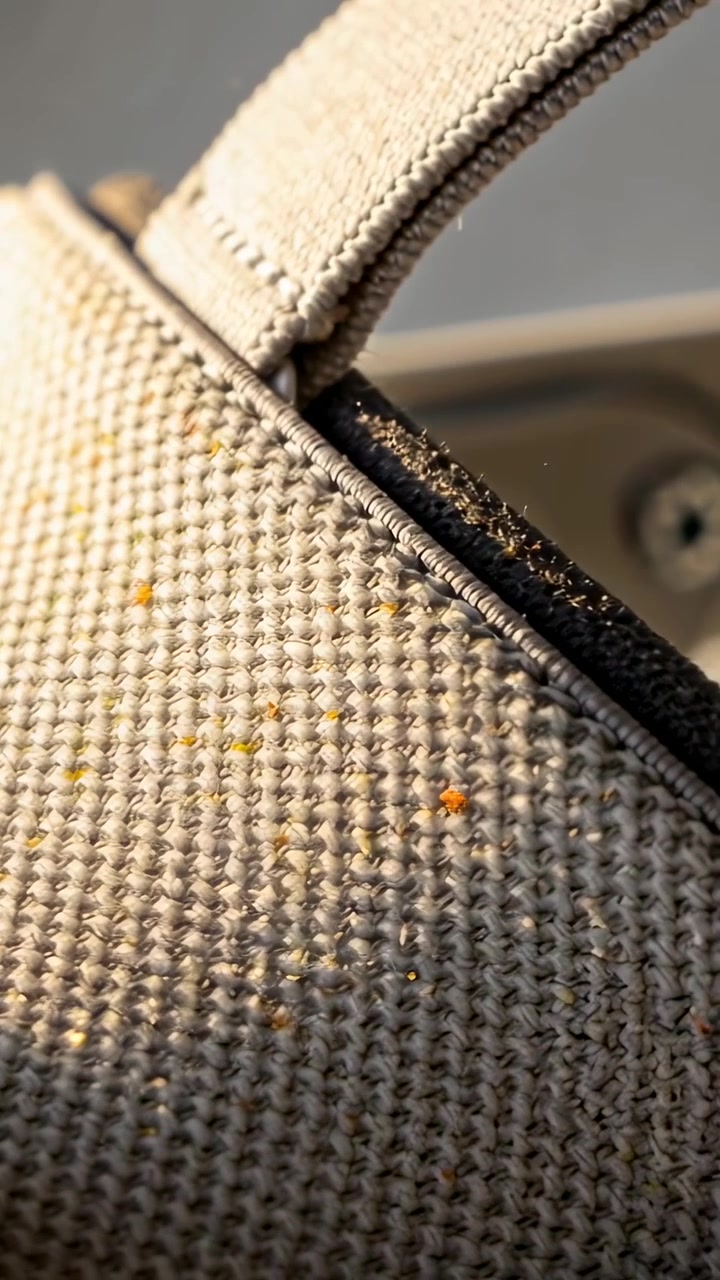 Video verticale: Telecamera che panoramica rivelando l'angolo di una borsa beige intrecciata in auto, con cucitura del cinturino e macchioline.