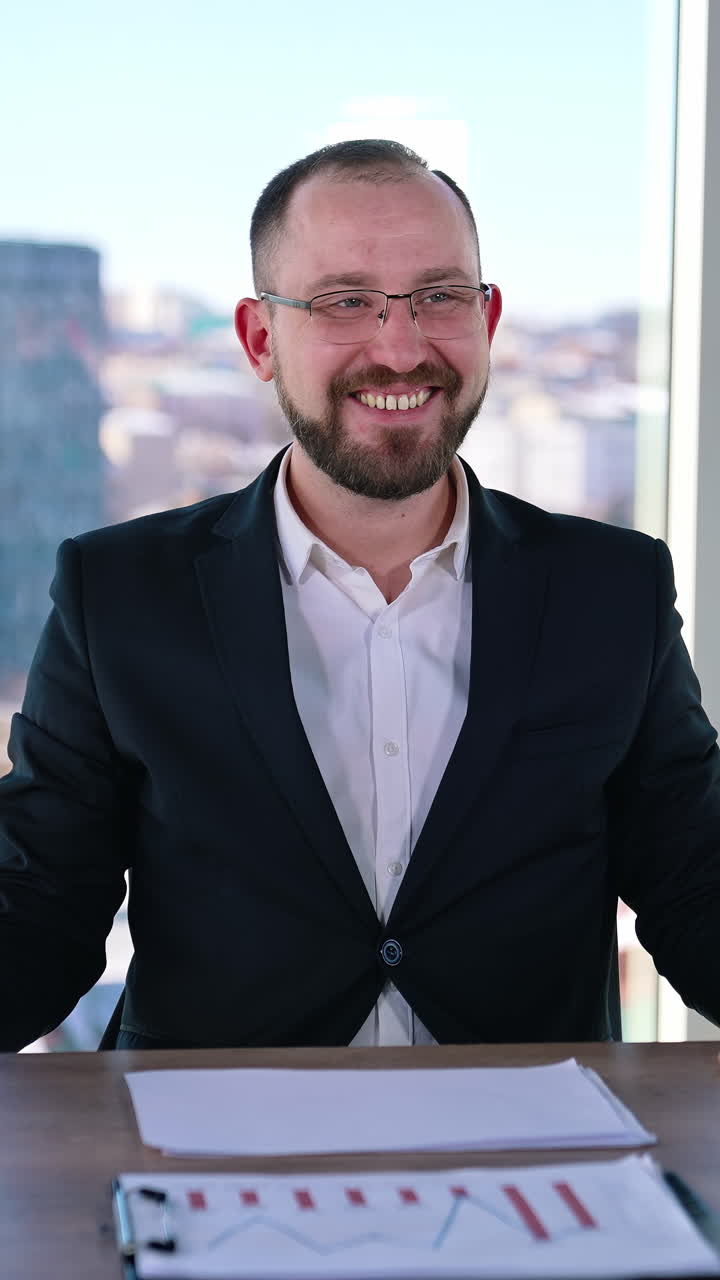 Astonished businessman at workplace. Smiling office worker sitting at the table with a laptop on window background with city view. Vertical video