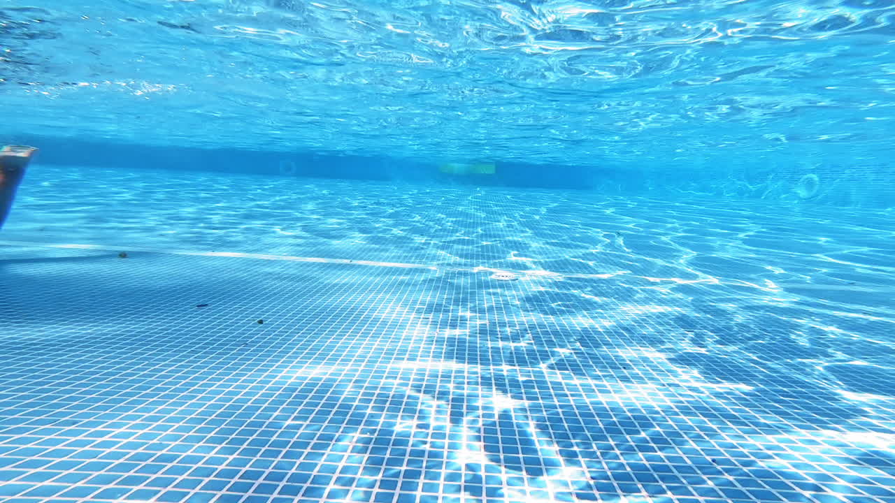 Empty swimming pool underwater with surface ripples. Bottom of the pool on the background of blue clear water inside.