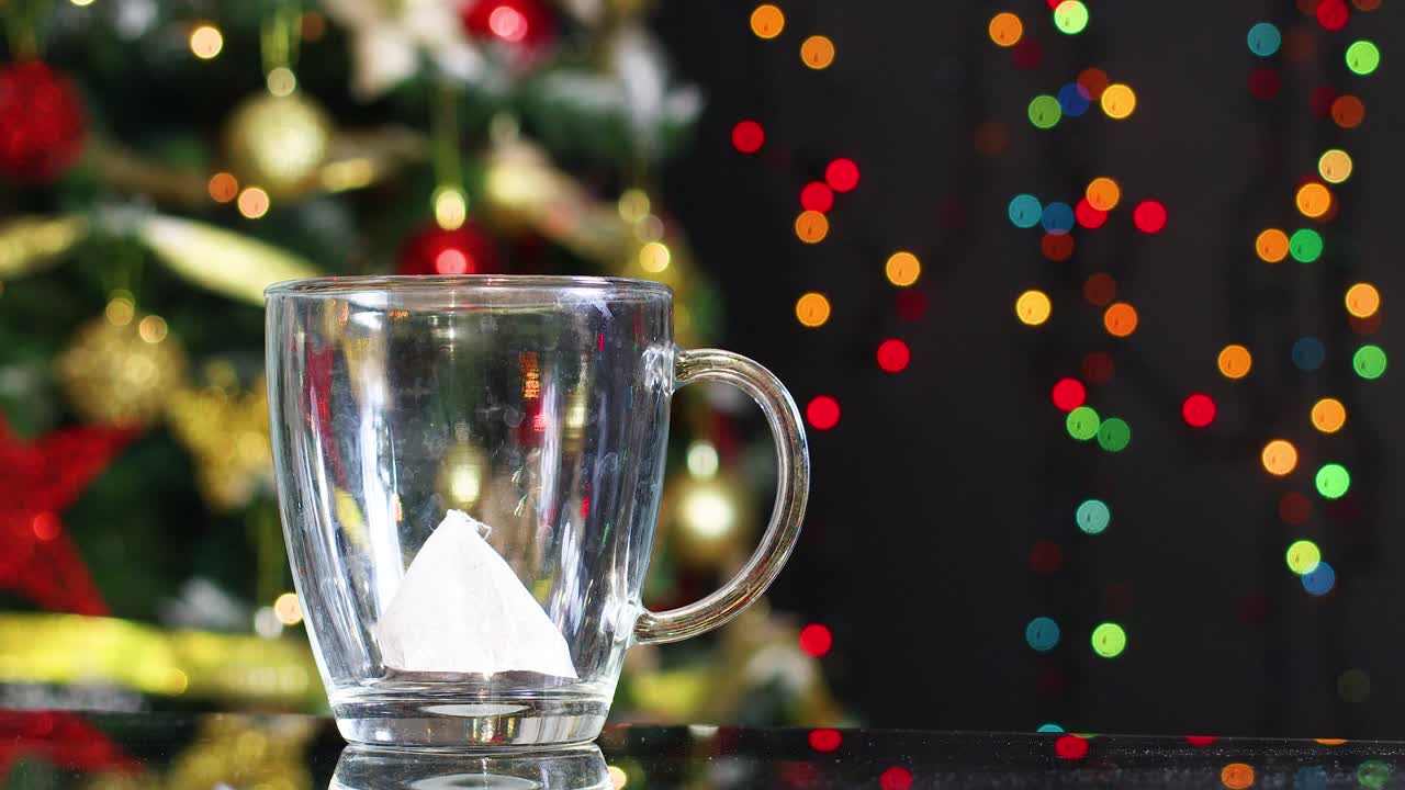 vertiendo té caliente en la taza con el árbol de navidad detrás