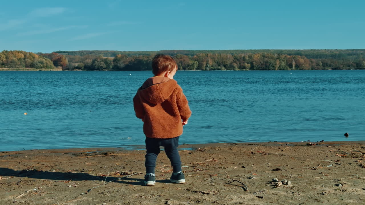 Joyful kid throwing stones into river. Adorable child spending time at the waterfront on sunny day.