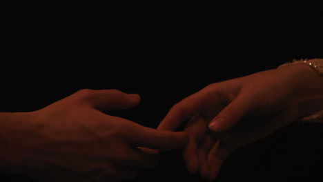 male - female fingers slowly touch against black background, close up