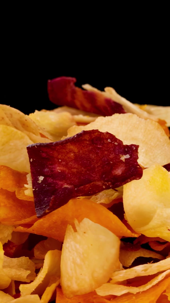Colorful root vegetable chips rotate under studio lighting, highlighting crispy textures and vibrant colors