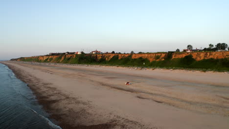 A-drone-aerial-shot-of-a-couple-sitting-on-a-beach-on-a-golden-sandy-beach-in-Norfolk,-Great-Britain