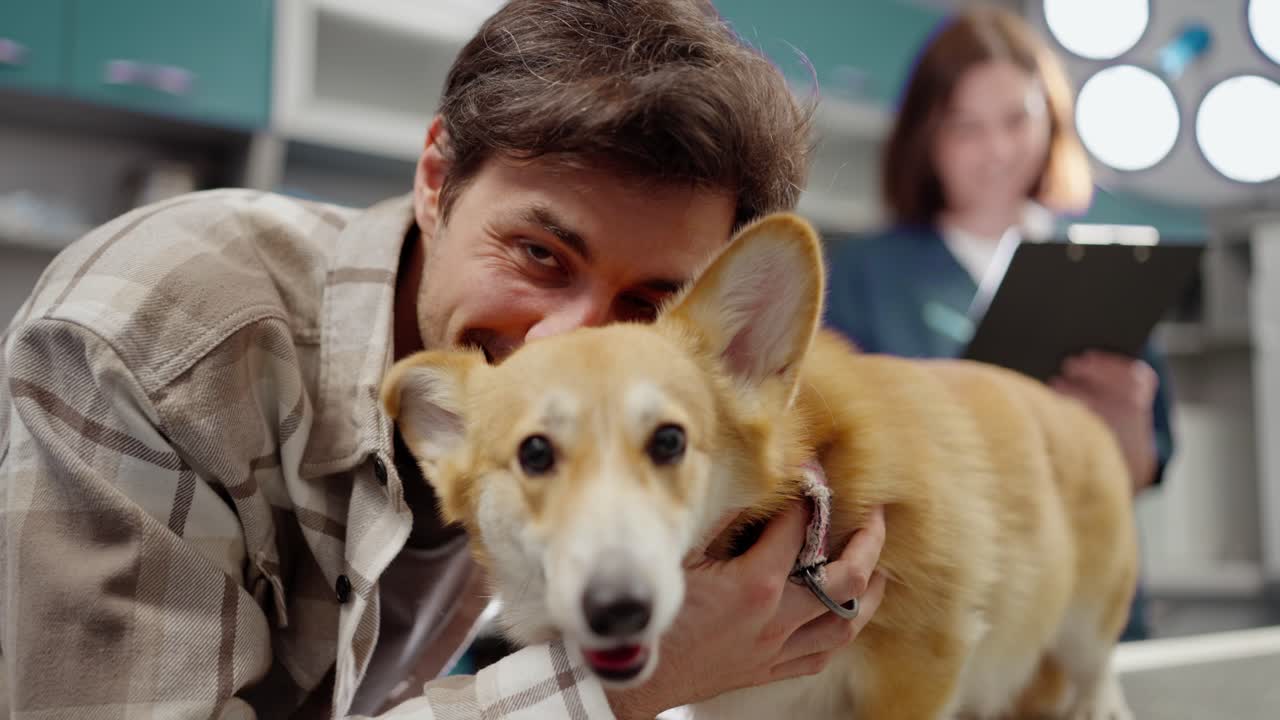 채색 셔츠를 입은 행복한 갈색 남자의 초상화. 수의사 클리닉의 수의사 사무실에서 노란색 색 코르기 개와 함께 포즈를 취하고 있다.