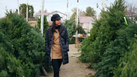 una mujer hermosa con un espíritu navideño feliz sonriendo mientras compra árboles de navidad festivos de abeto douglas