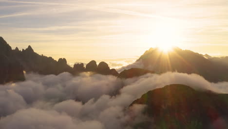 Golden-sunrise-silhouetted-South-Tyrol-Tre-Cime-mountains-surrounded-by-heavenly-clouds-aerial-rising-view