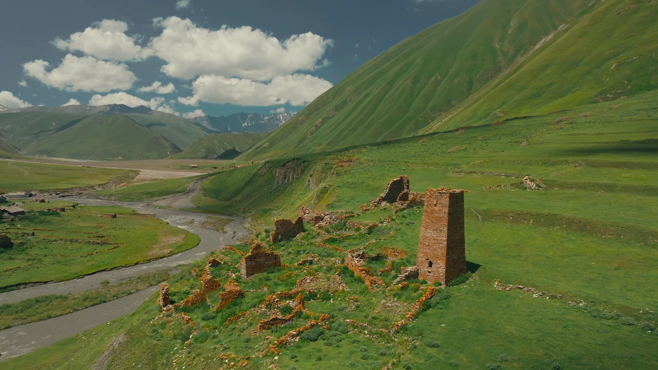 Drone close up orbit of a medieval fortress tower ruin in Truso Valley, Georgia, surrounded by green mountains and blue sky with cotton clouds, capturing history and landscape.