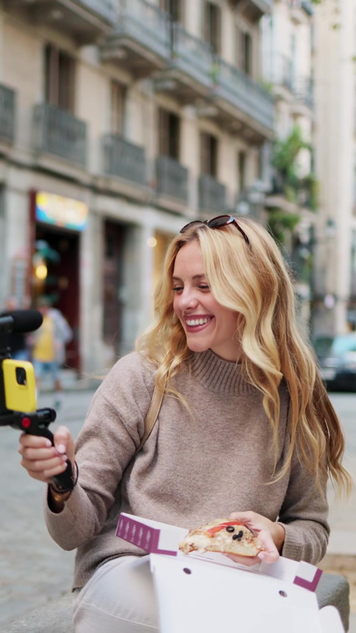 Donna sorridente che fa vlogging con lo smartphone e mangia la pizza