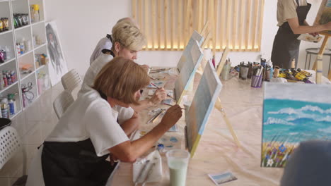 an old retired woman paints a picture together with friends. an elderly group of friends and a senior woman are drawing pictures together.