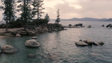 a man standing in the rocks of lake tahoe beautiful which is a large freshwater lake in the sierra nevada of the united states covered with tall pine trees, aerial clip