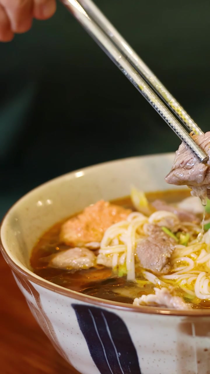 Primo piano di bacchette che prendono manzo dalla zuppa di noodle.