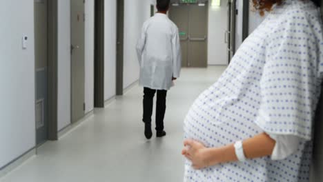 pregnant woman touching her belly while doctor walking in corridor