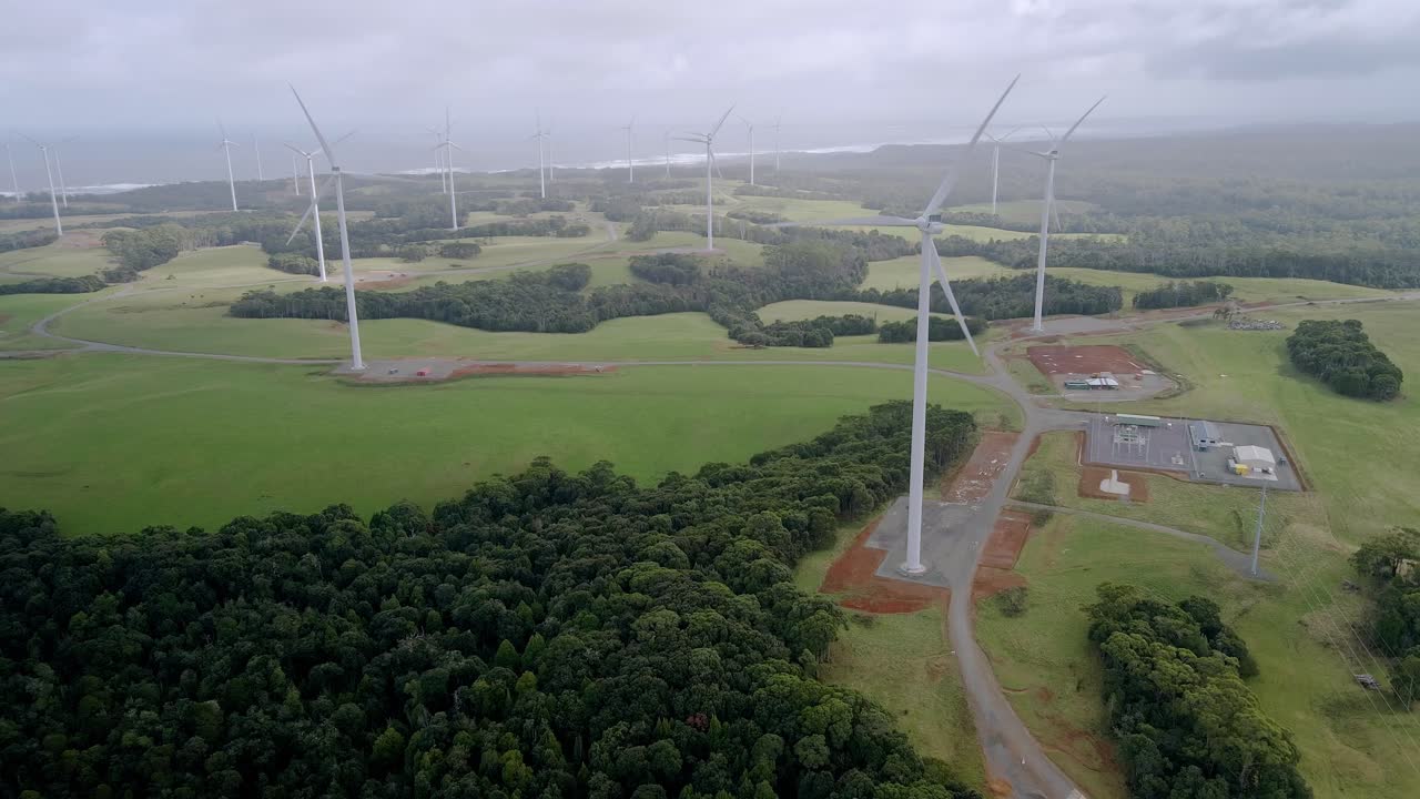 Reverse drone shot of rotating wind turbines on Tasmanian clean energy wind farm, Australia