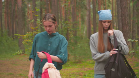 two young hikers walk through a serene forest, carrying backpacks, they approach a fallen tree as the lady in green starts to open her red bag