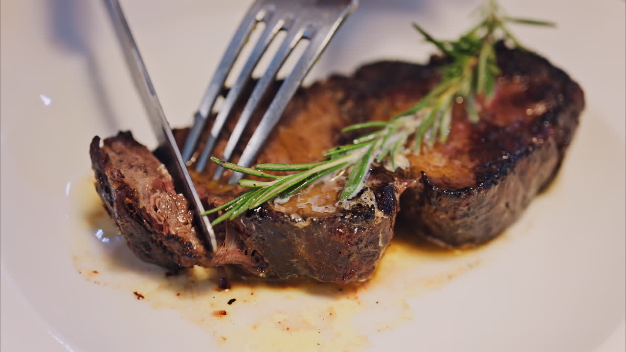 Close up of a woman cutting up a beef steak of with rosemary on a white plate at a restaurant