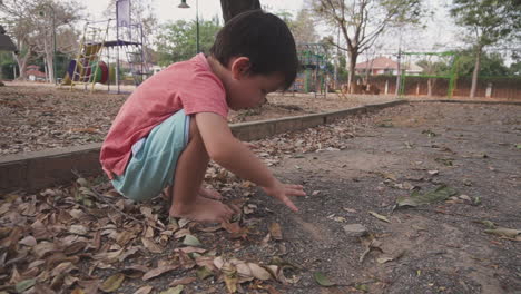 clip en cámara lenta de un niño asiático de dos años que se divierte jugando con la arena en un parque al aire libre ensuciándose las manos