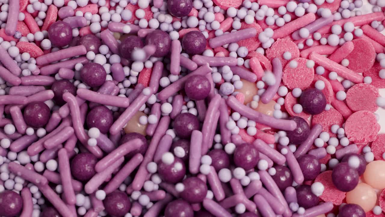Macro video of vibrant candies transitioning from pink to purple hues, showcasing a dynamic and colorful visual experience