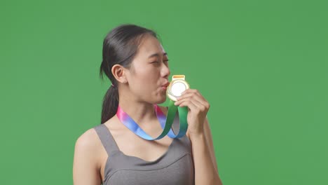 close up of asian woman kissing a gold medal in her hand being proud winning as the first winner on green screen background in the studio