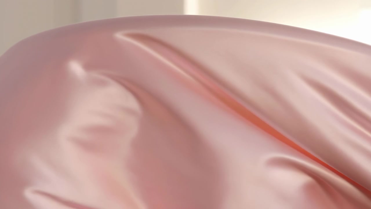 Primo piano di raso rosa liscio drappeggiato attraverso l'inquadratura, con delicati riflessi e un'illuminazione calda e soffusa che crea un elegante sfondo tessile astratto.