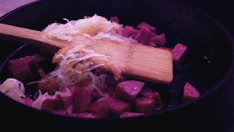 shredded cabbage added to cast iron pan with meat, cooking sauerkraut