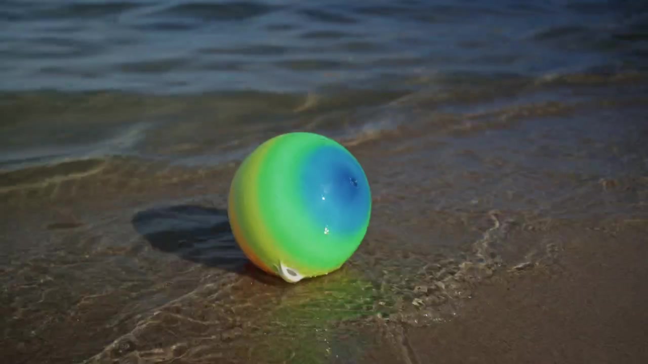 Bola pantai berwarna-warni mengambang di tepi ombak lembut di pantai berpasir Plage de la Gravette di Antibes, Prancis, pada hari musim panas yang cerah di French Riviera.