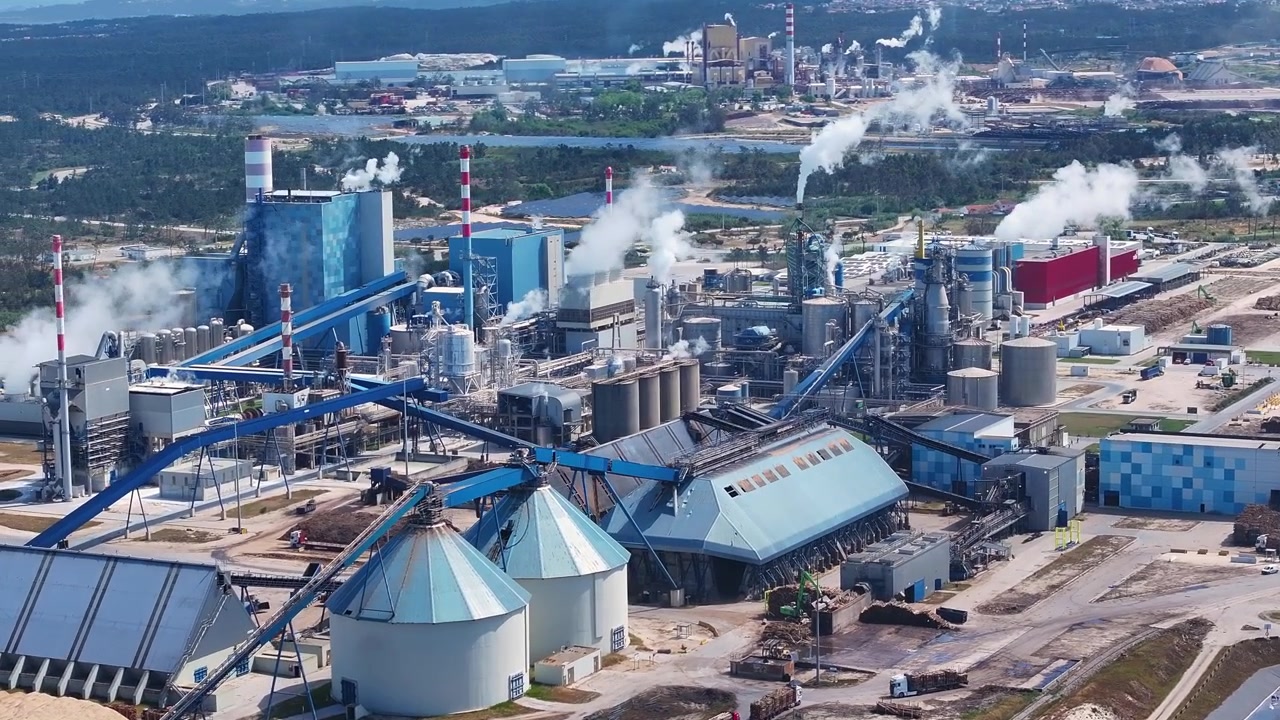 Expansive aerial perspective of a modern pulp and paper mill, showing the industrial complex with smoking chimneys and processing facilities