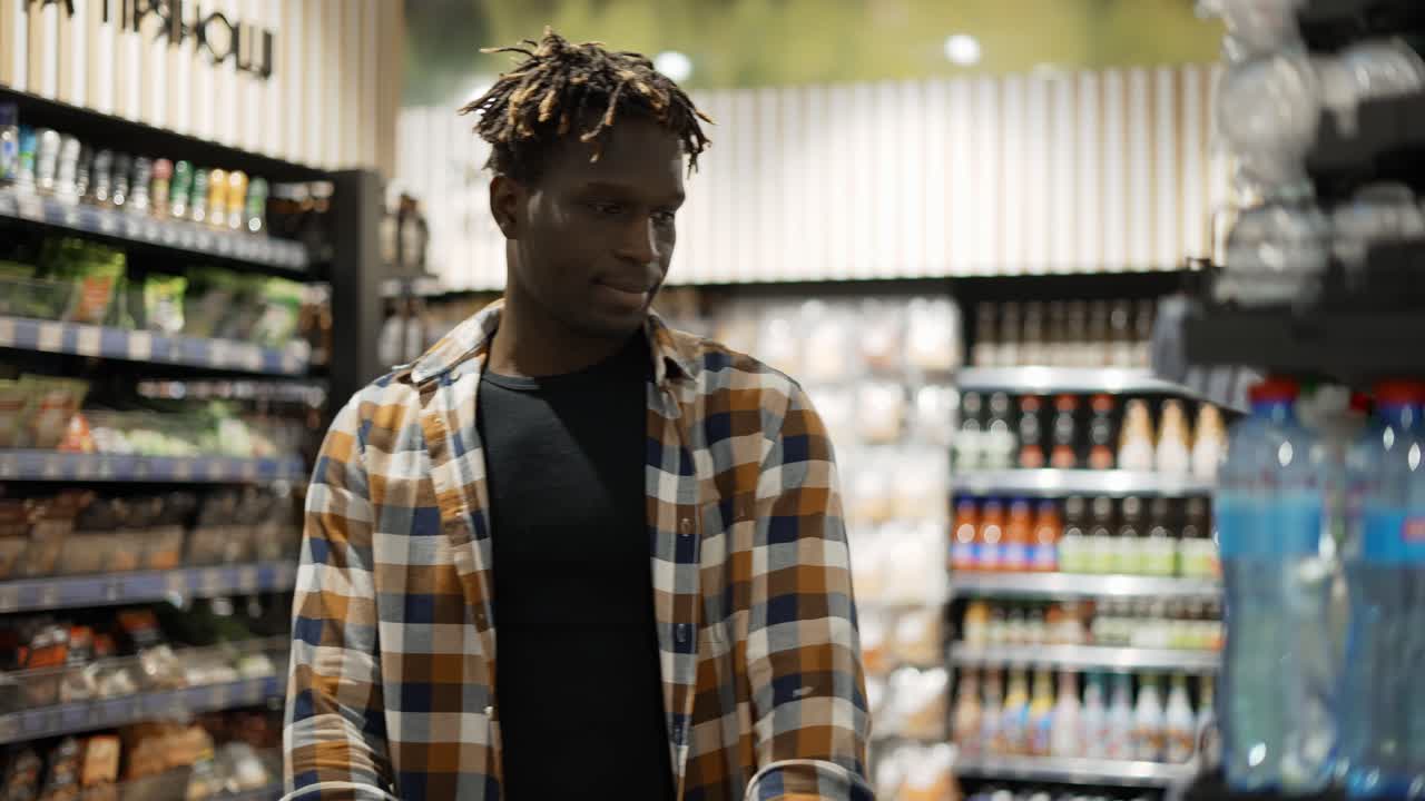 Un uomo spinge il carrello lungo il supermercato, prendendo una bottiglia d'acqua.