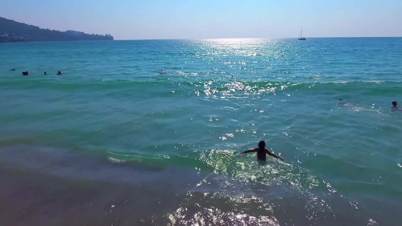 A low aerial view. A girl dives into the water while camera flies over her