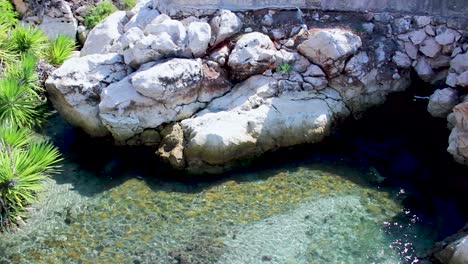 Slow-pan-footage-of-restaurant-on-the-cliffs-of-Greece-Kefalonia,-featuring-rock-formations,-a-small-inlet-and-palm-trees