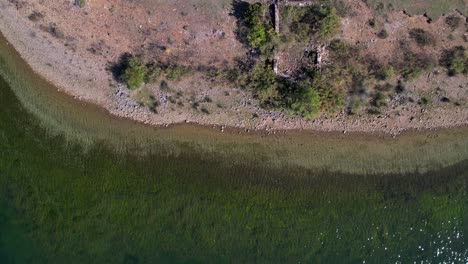 Green-water-of-calm-surface-lake-on-shore-see-from-above-in-mountains-near-ruins