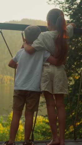 brother and sister enjoy glamping trip admiring scenic beauty of forest immersing in natural surroundings. boy and girl hug on balcony watching environment slow motion