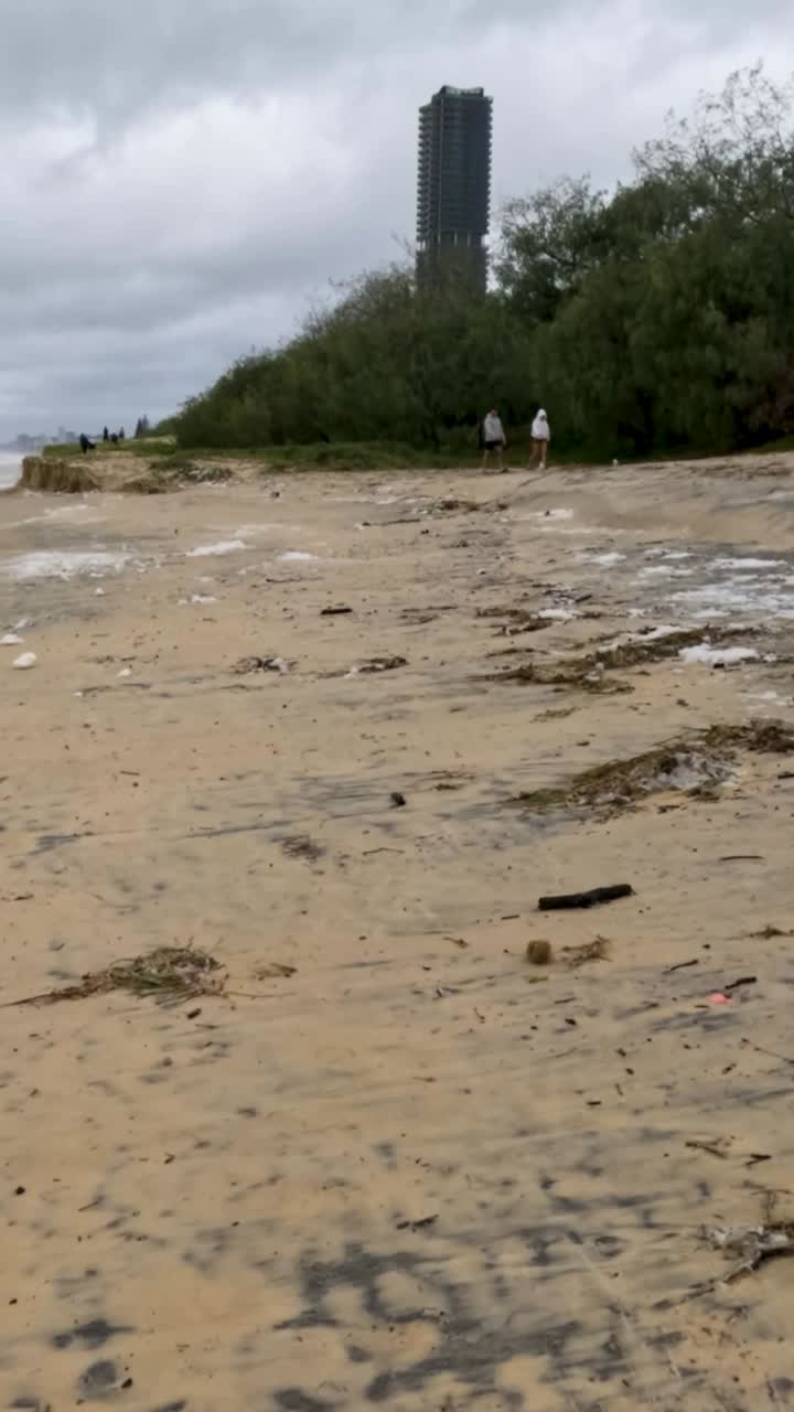 una escena de playa tormentosa muestra erosión y contaminación, con cielos nublados y olas turbulentas impactando la costa