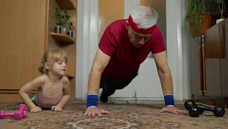 Aktiver-Großvater,-älterer-Mann-Mit-Kind,-Mädchen,-Das-Zu-Hause-Fitness-Liegestütze-Trainiert