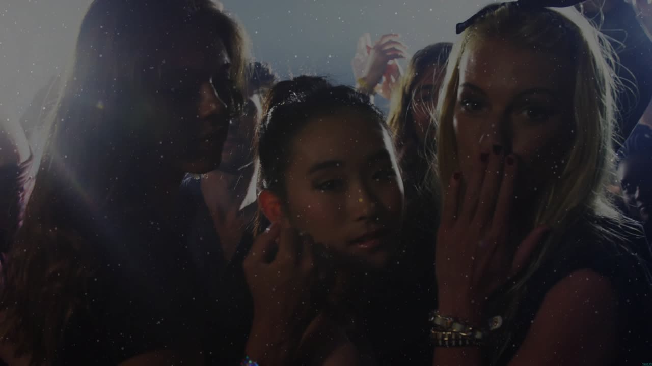 Sparkle overlay rising three women touching lips and blowing kisses, backlit crowd waving for music