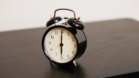 a black twin-bell analog alarm clock sits still, displaying 6:00 am. the classic bedside timepiece represents early mornings, punctuality, and the calm before the alarm rings.