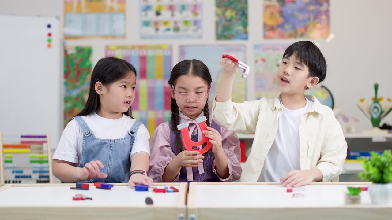 세 명의 초등학생이 밝고 부드러운 조명 아래 교실 책상에서 다채로운 자석으로 실험하는 모습, 고정 카메라