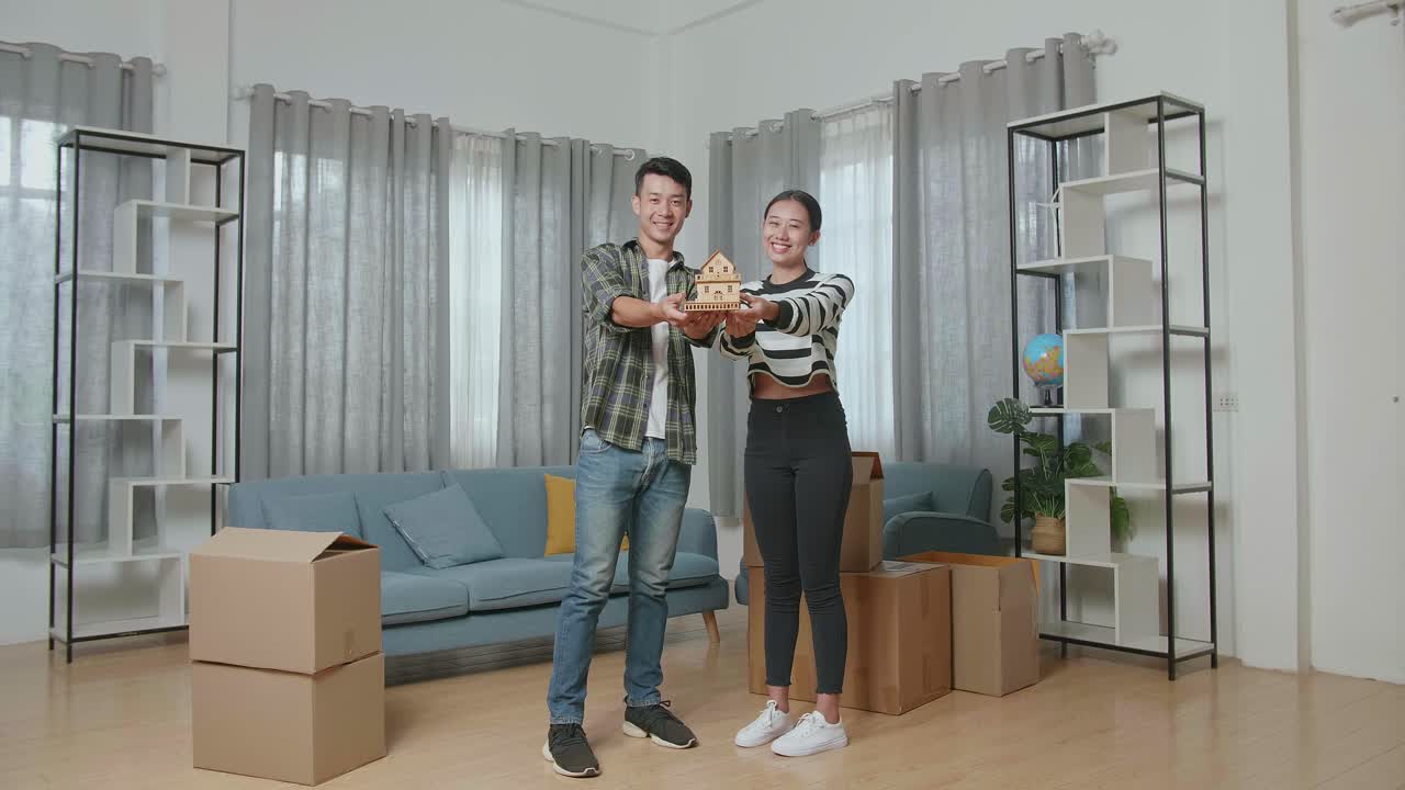 una pareja feliz sosteniendo una casa modelo en su nuevo hogar
