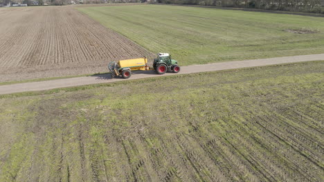 drone following tractor with large tank driving between green meadows